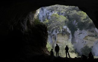 Panoramic-shot-of-silhouettes-at-a-caves-entrance-overlooking-a-bright-natural-valley