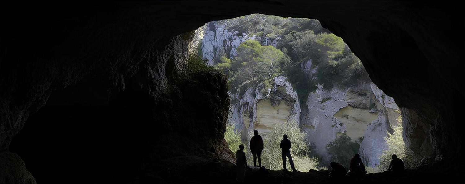 Panoramic-shot-of-silhouettes-at-a-caves-entrance-overlooking-a-bright-natural-valley